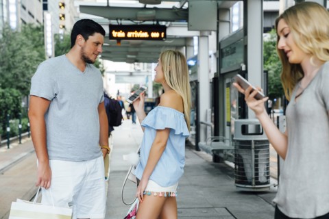 Caucasian woman showing cell phone to man at train station
