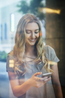 Smiling Caucasian woman texting on cell phone behind window