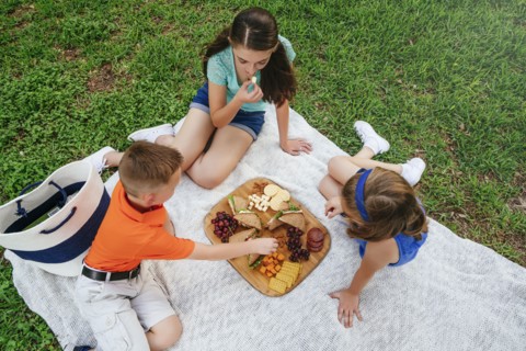 Caucasian brother and sisters eating snacks on picnic blanket