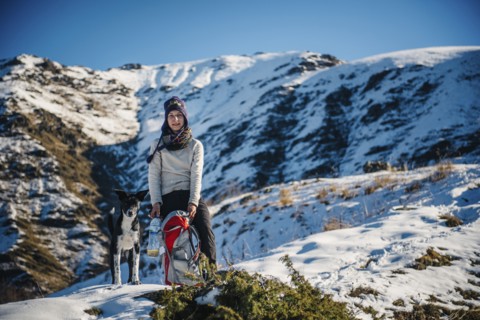 Caucasian woman posing with dog and backpack on mountain