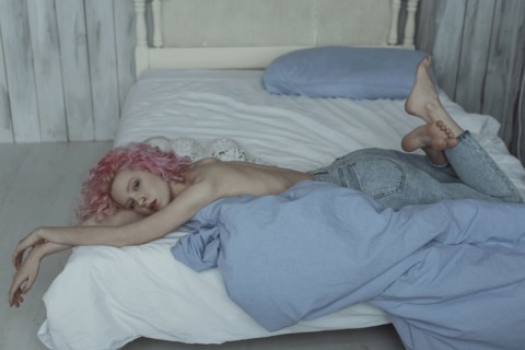 Topless Caucasian woman laying on bed wearing jeans