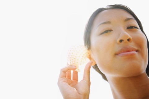 Asian woman listening to seashell