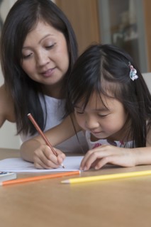 Asian mother watching daughter coloring