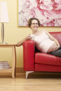 Caucasian pregnant woman having cup of coffee on sofa