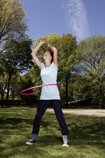 Mixed race woman spinning with plastic hoop in park
