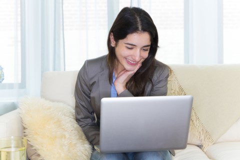 Hispanic woman using laptop on sofa
