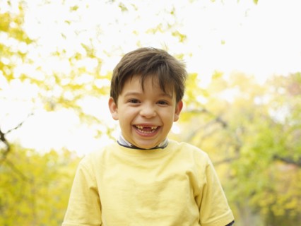 Toothless Hispanic boy grinning outdoors in autumn