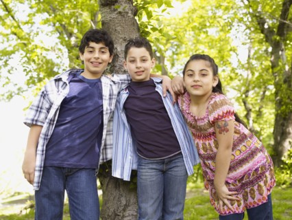 Mixed race boys and girl hugging in front of tree