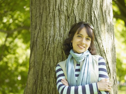 Smiling Hispanic woman leaning against tree with arms crossed