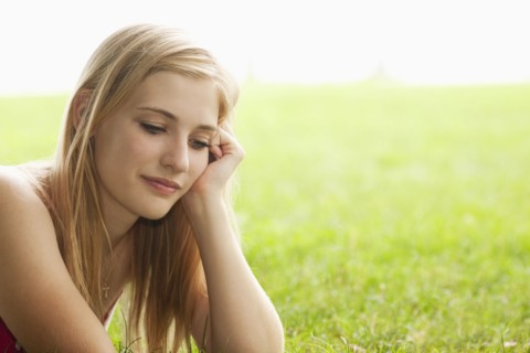 Serious Caucasian teenage girl sitting in grass