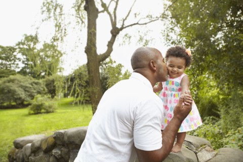 Mixed race father kissing daughter in park
