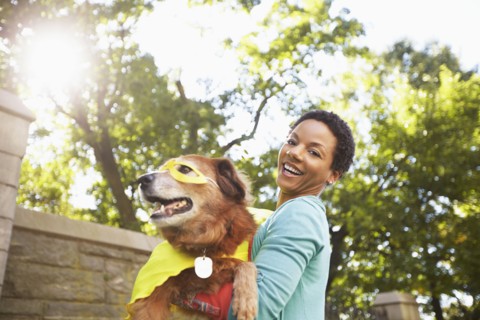Black woman carrying costumed dog in park