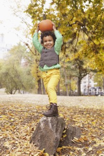 Mixed race boy holding pumpkin overhead in park