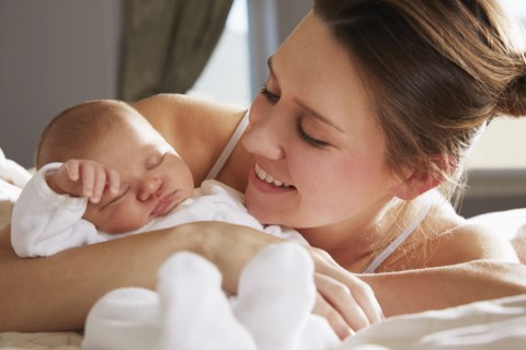 Mother hugging newborn baby on bed
