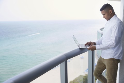 Black businessman using laptop on balcony