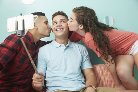 Smiling friends taking selfie kissing cheeks of man