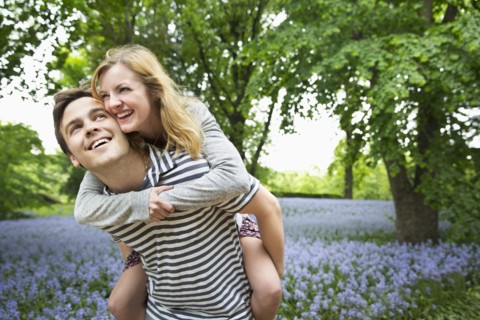 Caucasian man carrying girlfriend piggyback in field of flowers