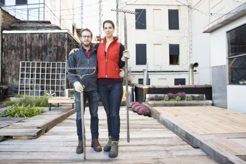 Couple holding rakes in urban rooftop garden