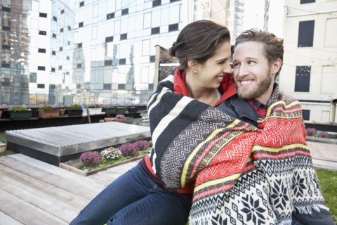 Couple wrapped in blanket on urban rooftop