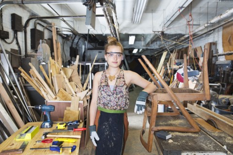 Caucasian woman leaning on wooden chair in workshop