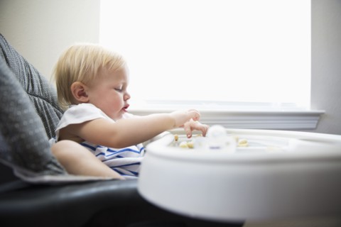 Caucasian baby girl self-feeding in high chair