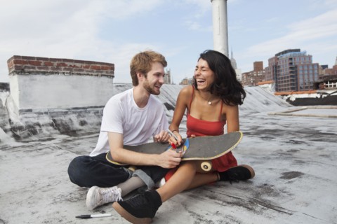 Mixed Race couple sitting on rooftop with skateboard