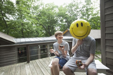 Caucasian father and son eating donuts with smiley face balloon