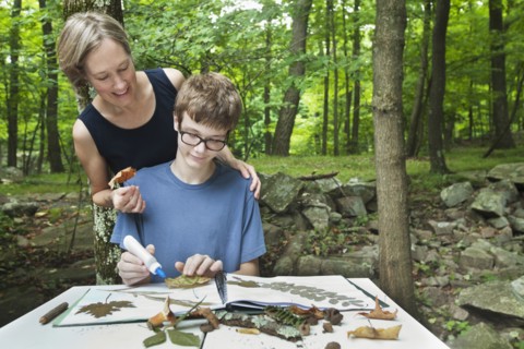 Caucasian mother watching son with nature scrapbook outdoors