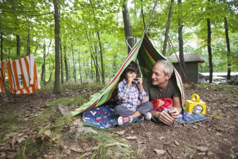 Father watching son playing harmonica in blanket fort