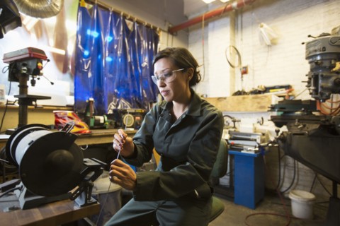 Mixed Race woman holding metal rod in workshop