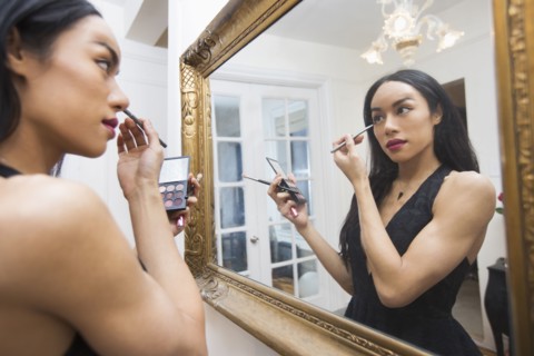 Glamorous transgender Thai woman applying eyeliner in mirror