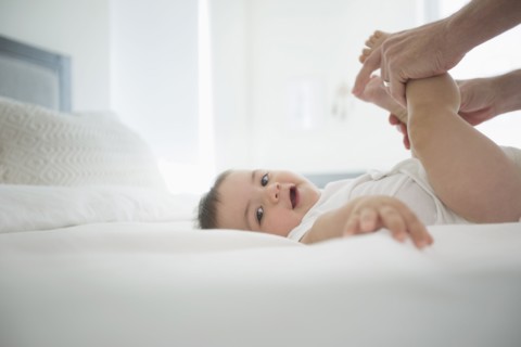 Father holding legs of baby son on bed