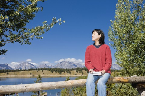 Japanese woman sitting on fence with mountains in background