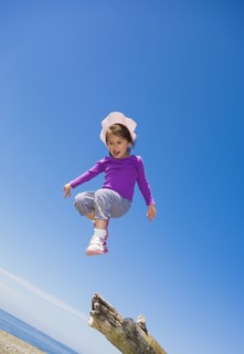 Low angle view of mixed race girl jumping from log on beach