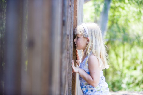 Curious Caucasian girl peeking through wooden fence