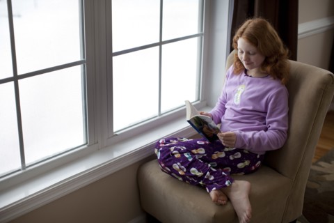 Caucasian girl reading on book near window