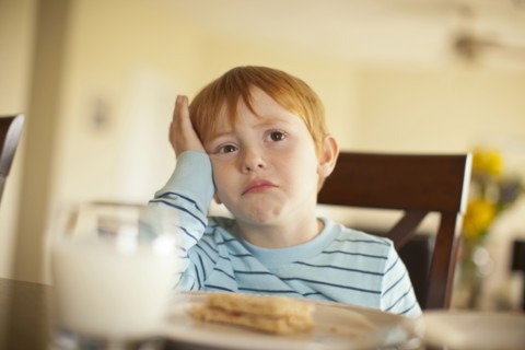 Caucasian boy pouting at dinner table