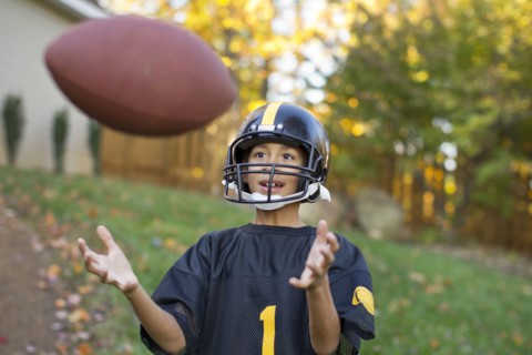 Mixed race boy playing football outdoors