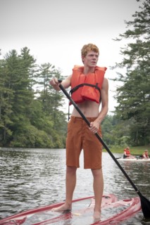 Caucasian teenage boy rowing paddleboat in lake