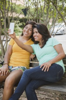 Hispanic mother and daughter posing for cell phone selfie