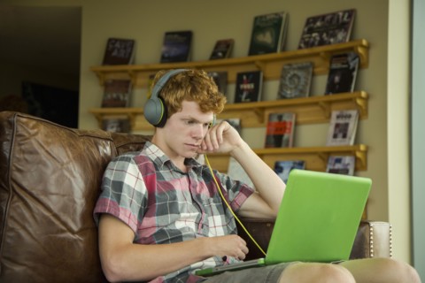 Caucasian boy sitting on sofa listening to laptop with headphones