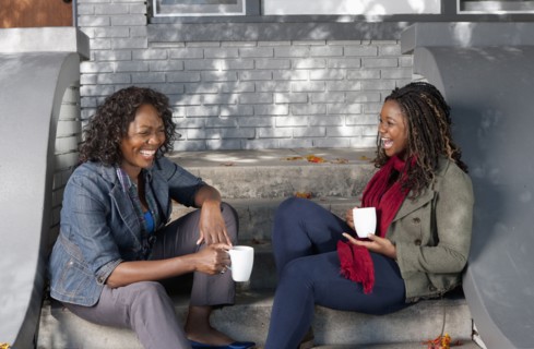Black mother and daughter sitting on front stoop drinking coffee