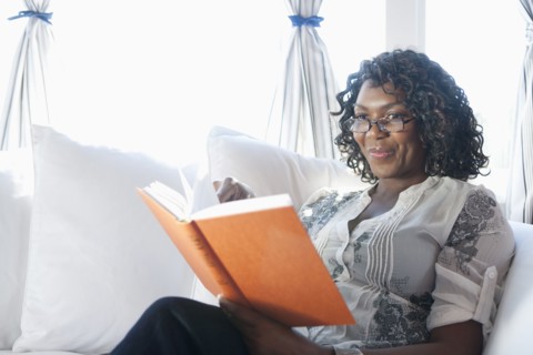 Black woman reading book on sofa