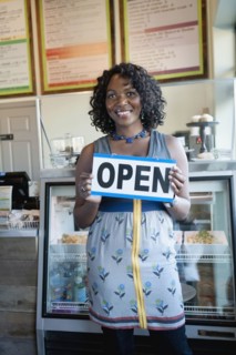 Black woman holding open sign in bakery