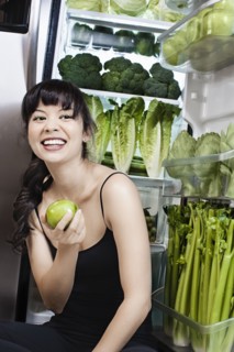 Mixed race woman with apple near green vegetables in refrigerator