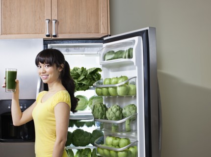 Mixed race woman drinking healthy drink near refrigerator