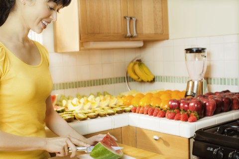 Mixed race woman cutting watermelon in kitchen