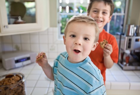 Caucasian brothers sneaking cookies in kitchen