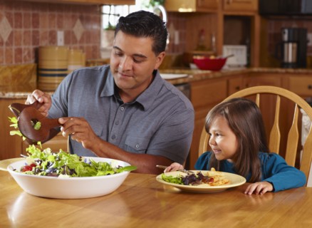 Father serving daughter salad at dinner table