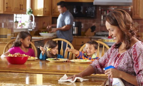 Mother cleaning while children eat in background